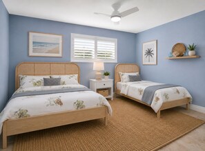 A bedroom with two beds, a ceiling fan, a window with blinds, and a wall-mounted shelf with decorative items. - Newly renovated 2-bedroom condo in charming Sanibel with views of the river. (Sanibel)