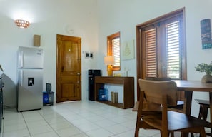 A compact kitchen with a refrigerator, microwave, and a water dispenser. There is a wooden door, a table with chairs, and a window with blinds. - Condominio a solo unos pasos de la hermosa playa con gran piscina!! (Las Terrenas)