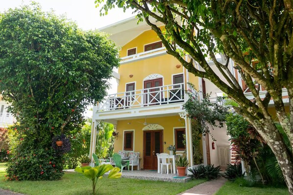 A two-story building with a balcony, surrounded by lush greenery and a well-maintained lawn. - Condominio a solo unos pasos de la hermosa playa con gran piscina!! (Las Terrenas)
