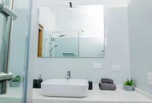 A modern bathroom with a large mirror, a white sink, a shower, and a potted plant. - Condominio a solo unos pasos de la hermosa playa con gran piscina!! (Las Terrenas)