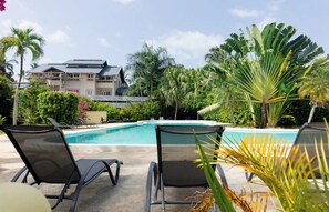 A pool area with lounge chairs, a building in the background, and tropical vegetation. - Condominio a solo unos pasos de la hermosa playa con gran piscina!! (Las Terrenas)