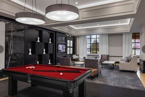 A modern living room with a pool table, comfortable seating, and a large window providing a view of the city. - Marriott Grand Chateau Studio- King Bed, Sofa Bed, Kitchenette on F1 Race Route (Las Vegas)