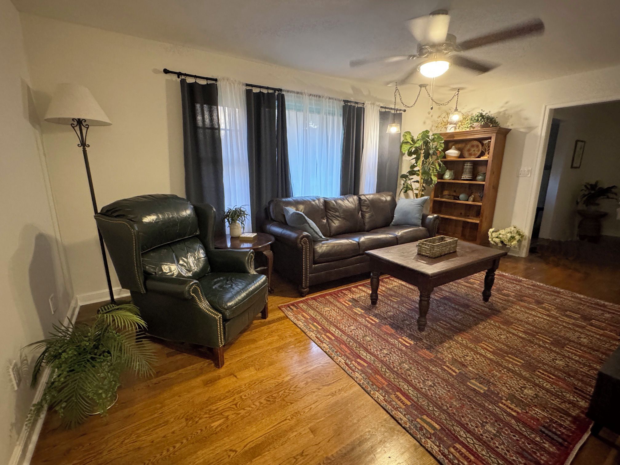 A living room with a leather armchair, a sofa, a coffee table, and a bookshelf.