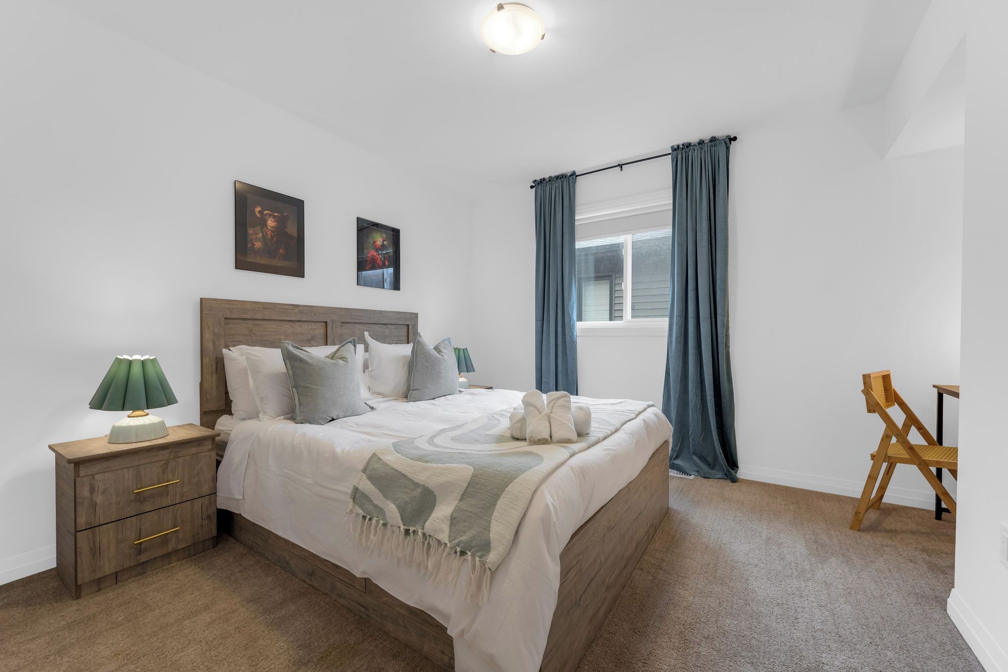 A bedroom with a bed, bedside tables, a lamp, a window with curtains, and artwork on the wall.