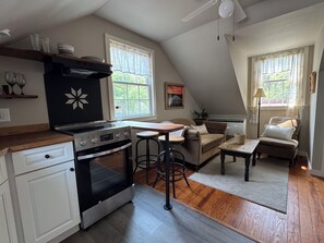 A compact kitchen with a stove, oven, and bar stools. There is a dining area with a table and a sofa.