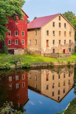 Ein historisches Gebäude mit einem roten Bauernhaus und einem Steinbau, das sich in ruhigem Wasser spiegelt.