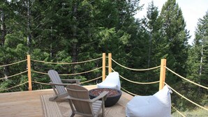 En träaltan med två Adirondack-stolar och en eldstad, omgiven av ett avspärrningsrep och en tät skog.
