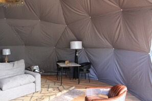 A tented accommodation with a sofa, a table with chairs, and a lamp.