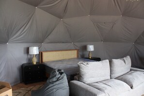 Een ingerichte tent met een bed, twee nachtkastjes met lampen, een bank en een koffer.