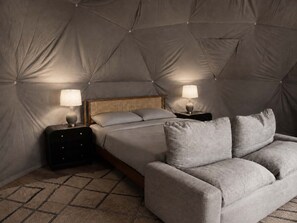 Een slaapkamer met een bed, twee nachtkastjes met lampen, een bank en een kamerbreed tapijt met een patroon.
