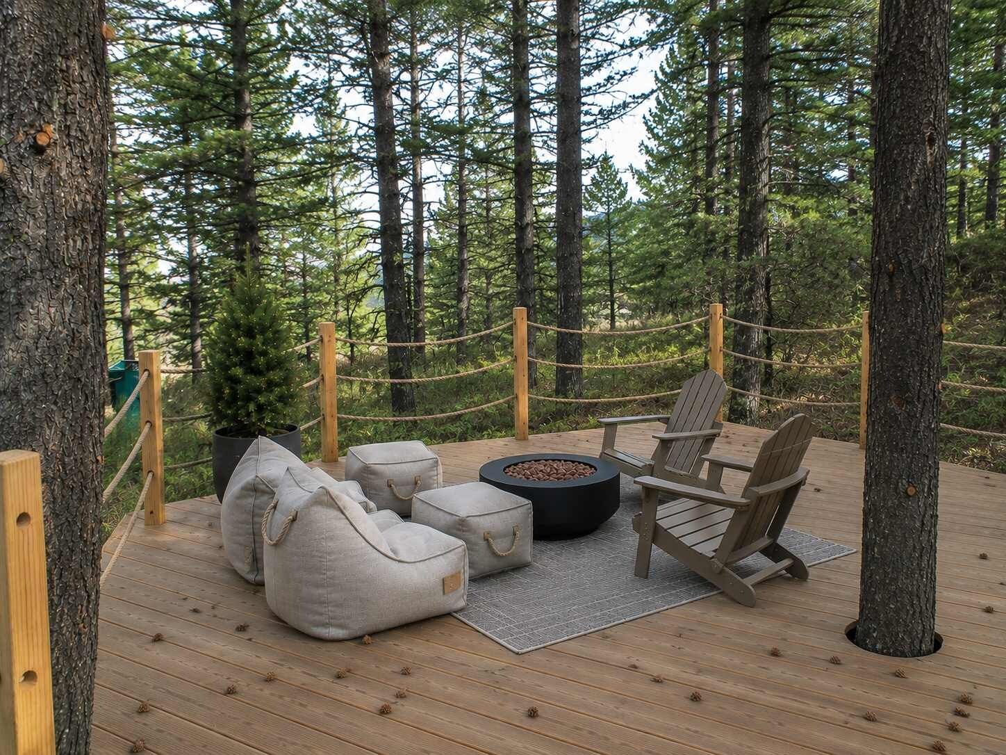 Une terrasse avec coin salon extérieur, comprenant un foyer, des chaises et des coussins, le tout entouré d’arbres.