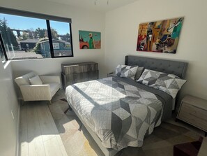 Une chambre à coucher avec un lit, une chaise, une commode et deux tableaux accrochés au mur.