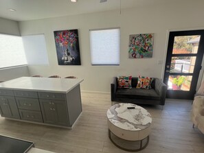 A modern living room with a grey sofa, a round coffee table, and a kitchen area with grey cabinets. - Tranquil 1-bedroom house in beautiful Capitola near the beach (Capitola)