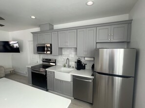 A modern kitchen with grey cabinets, stainless steel appliances, and a flat-screen TV mounted on the wall. - Tranquil 1-bedroom house in beautiful Capitola near the beach (Capitola)