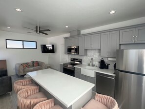 A modern kitchen with grey cabinets, a stainless steel refrigerator, a flat-screen TV, and a central island with seating. - Tranquil 1-bedroom house in beautiful Capitola near the beach (Capitola)