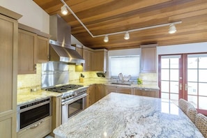 A kitchen with wooden cabinets, a stainless steel range hood, a granite countertop, and a large island. - Luxury Ocean-View 2-bedroom Condo Across from Beach (Redondo Beach)