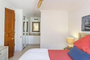 Ein Schlafzimmer mit einem Bett, einem Nachttisch mit Lampe, einer Tür und Blick ins Badezimmer.