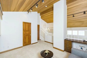 A room with a wooden ceiling, a staircase, a kitchen area, and a round table with a sculpture. - Luxury Ocean-View 2-bedroom Condo Across from Beach (Redondo Beach)