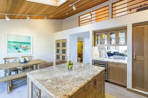A modern kitchen with a marble countertop, wooden cabinets, and a dining area with a bench. - Luxury Ocean-View 2-bedroom Condo Across from Beach (Redondo Beach)