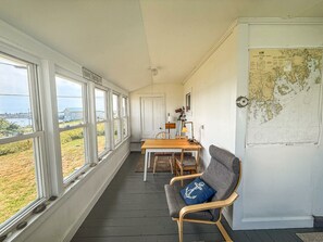 A room with a long window wall, a dining table with chairs, a sofa with a cushion, and a map on the wall. - A working waterfront cottage in Downeast Maine, trails and beaches nearby (Jonesport)