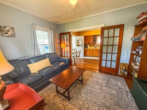 A living room with a sofa, coffee table, and a patterned rug. There is a kitchen visible through an open doorway. - A working waterfront cottage in Downeast Maine, trails and beaches nearby (Jonesport)