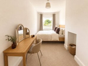A bedroom with a bed, a bedside table, a chair, a mirror, a window with curtains, and a small plant.