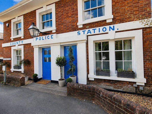 A police station with a blue door, a sign reading 'COUNTY POLICE STATION,' and potted plants outside.