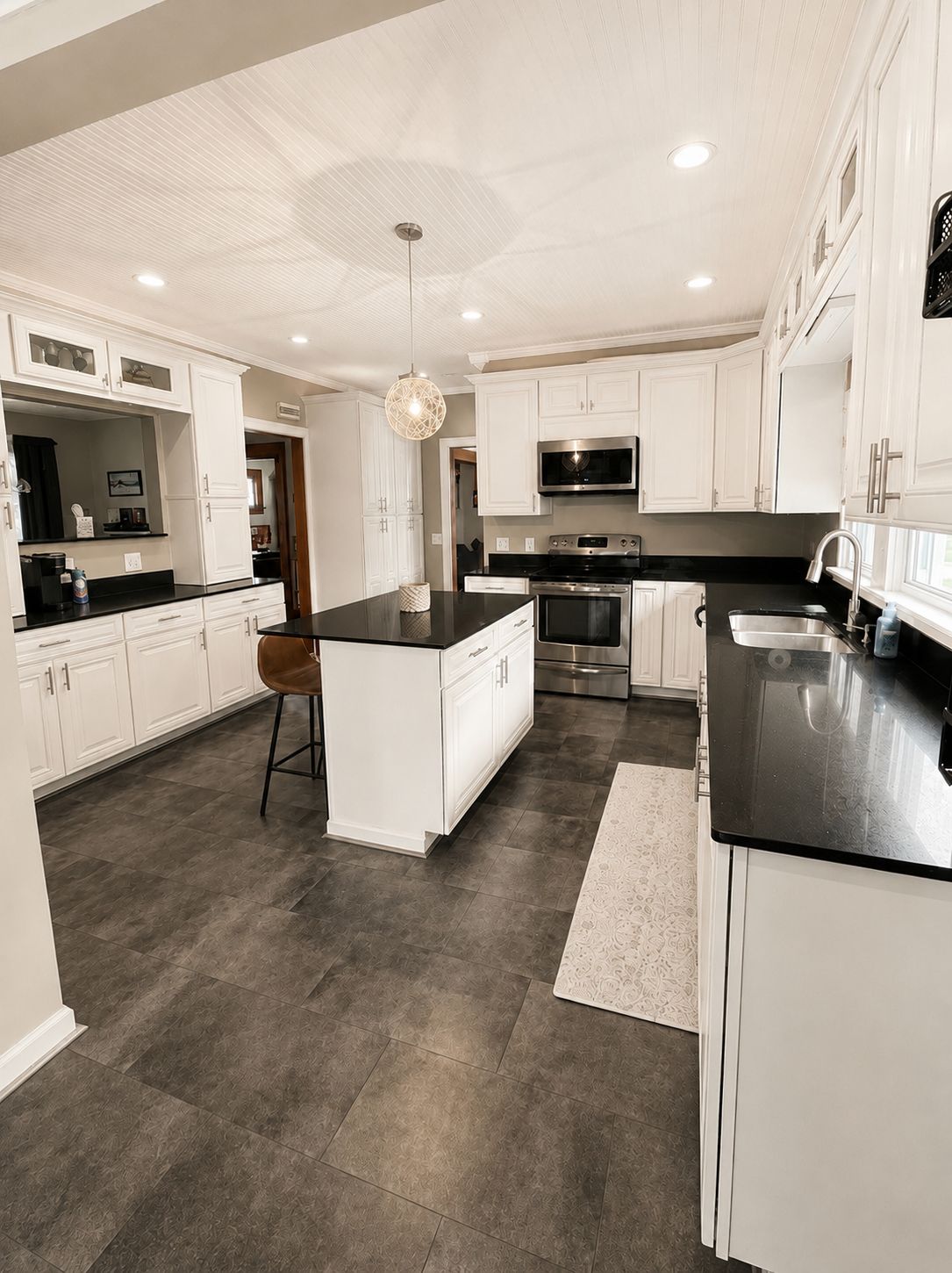 A modern kitchen with white cabinetry, a central island, stainless steel appliances, and a patterned rug.