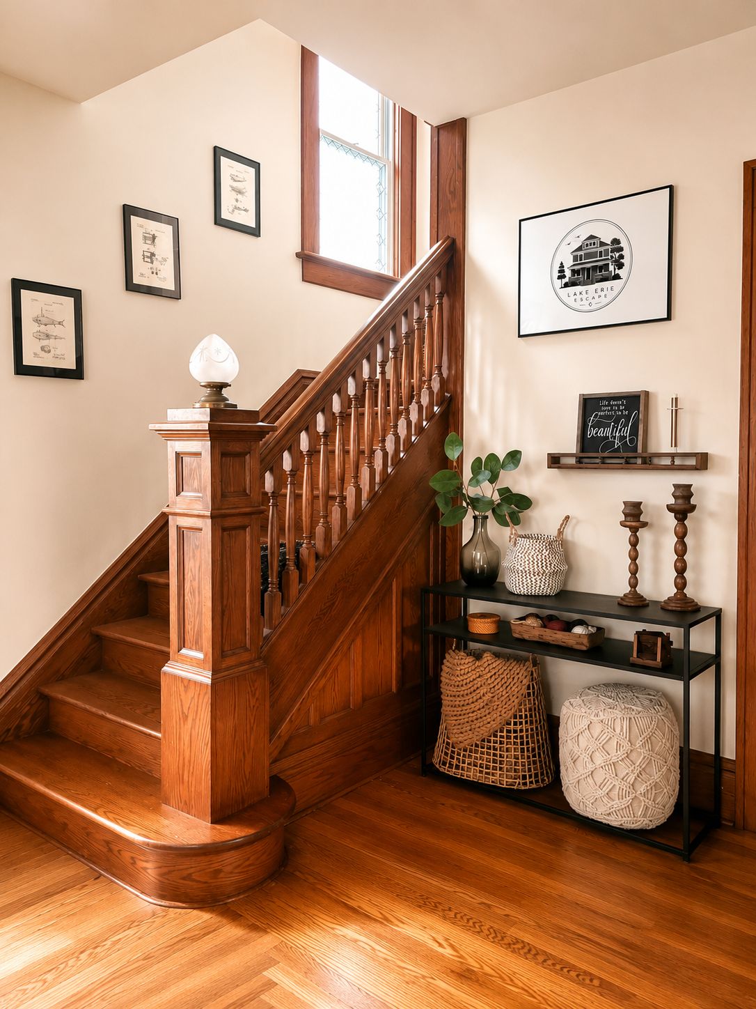 Un escalier en bois avec une rampe, un mur orné de tableaux encadrés et une étagère avec des objets décoratifs.
