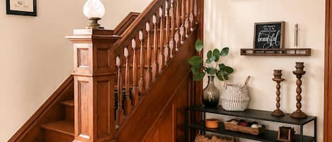 Un escalier en bois avec une rampe, un mur orné de tableaux encadrés et une étagère avec des objets décoratifs.