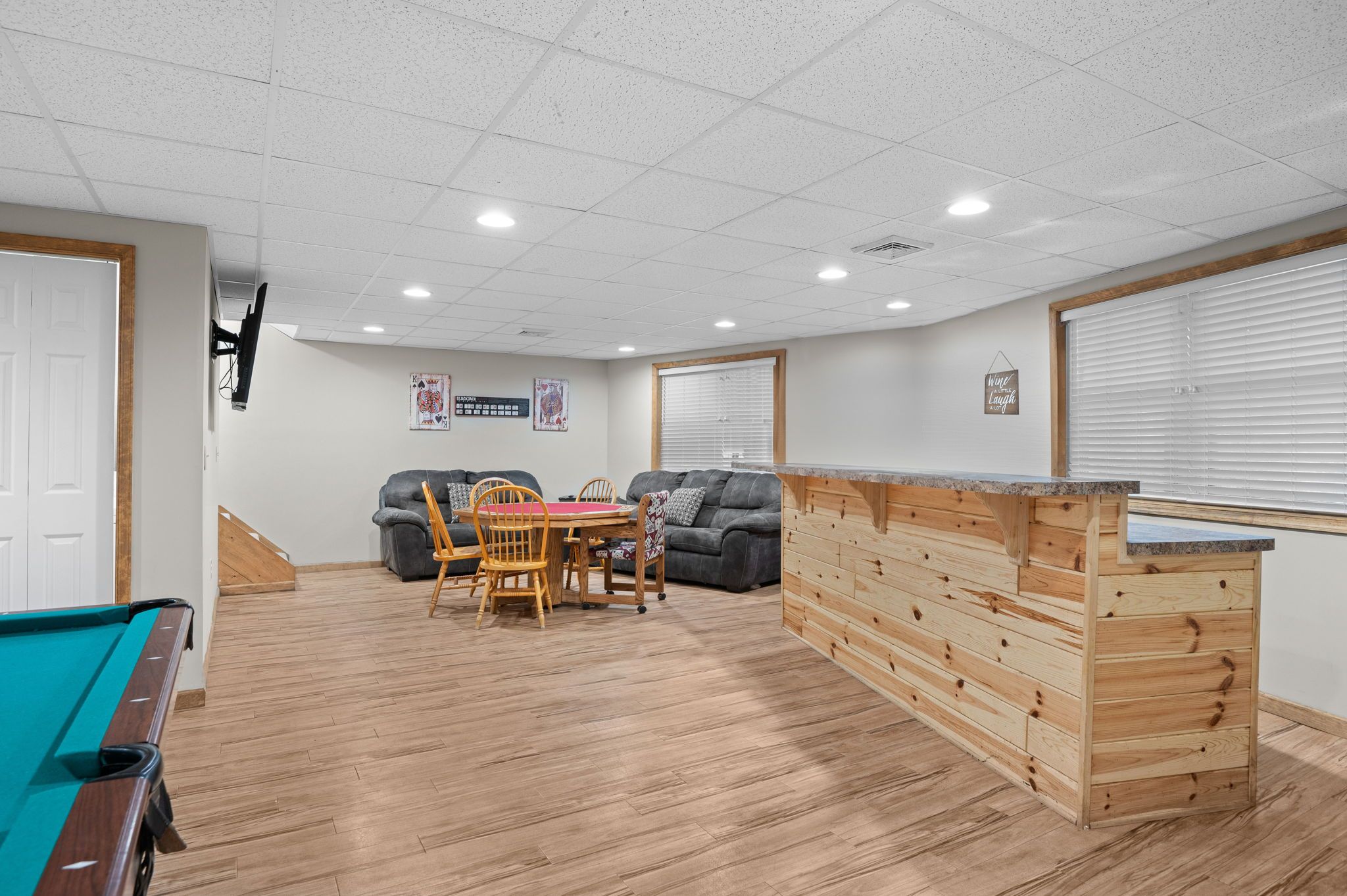 Een kamer met een pooltafel, een houten bar, een eettafel met stoelen en twee banken.