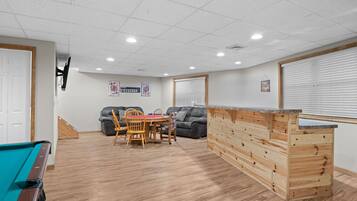 Een kamer met een pooltafel, een houten bar, een eettafel met stoelen en twee banken.