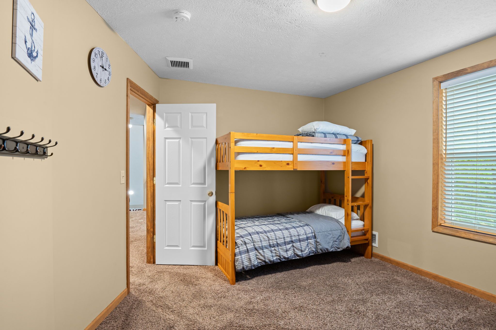 A room with a bunk bed, a door, a clock, and a window with blinds.