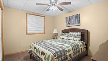 A bedroom with a bed, a ceiling fan, a window with blinds, a bedside lamp, and a wall-mounted picture.