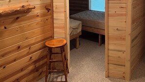 A wooden cabin room with a single bed, a small stool, and a thermostat on the wall. - Hunters Haven- 4 bedrooms, 1 bath with a separate bar/TV room to relax (Lidgerwood)