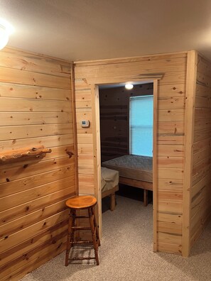 A wooden cabin room with a single bed, a small stool, and a thermostat on the wall. - Hunters Haven- 4 bedrooms, 1 bath with a separate bar/TV room to relax (Lidgerwood)