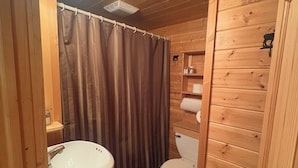 A wooden cabin bathroom with a white sink, toilet, and shower curtain. - Hunters Haven- 4 bedrooms, 1 bath with a separate bar/TV room to relax (Lidgerwood)