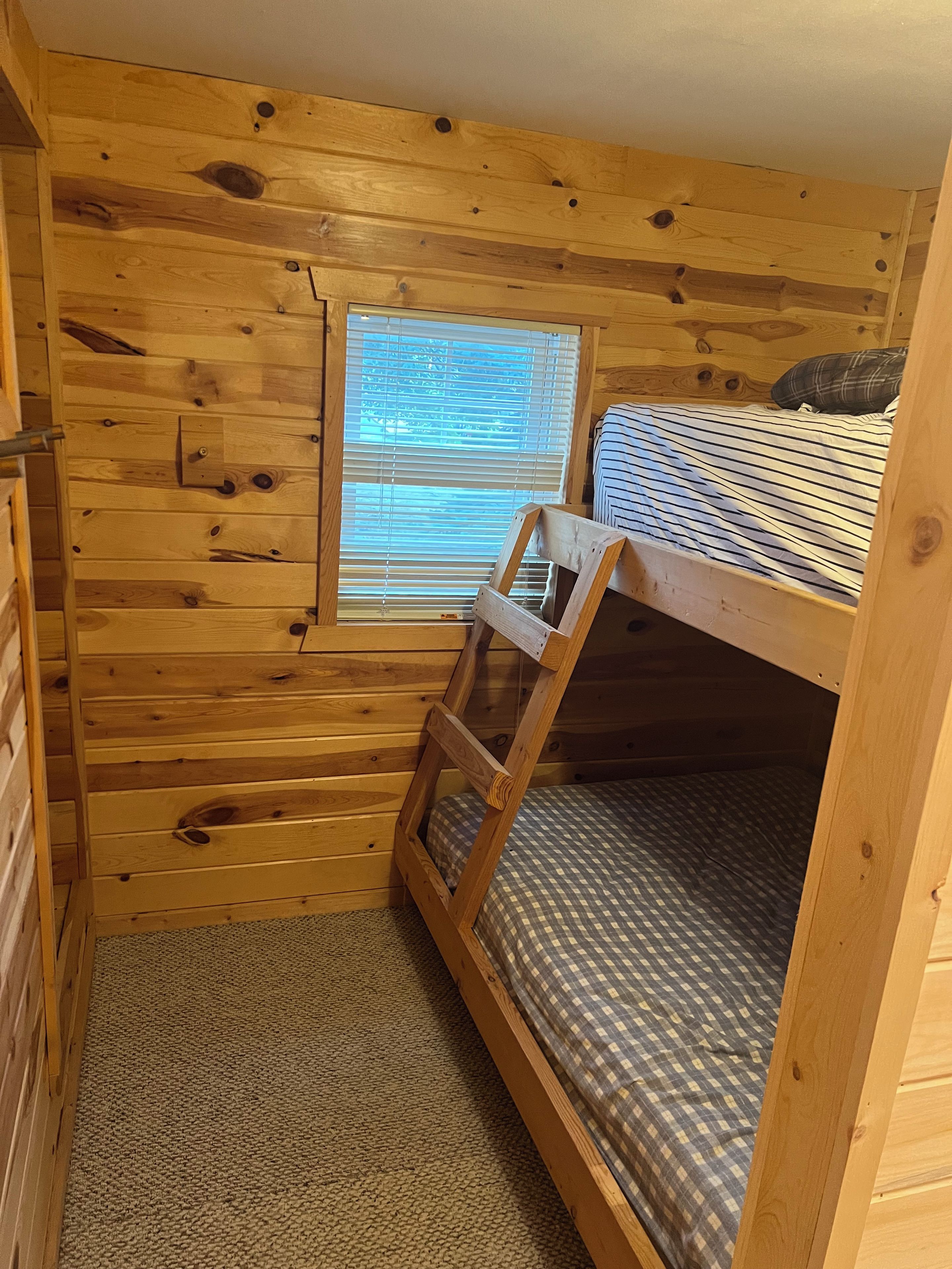 Una stanza in legno con un letto a castello, una finestra con persiane e un pavimento rivestito di moquette.