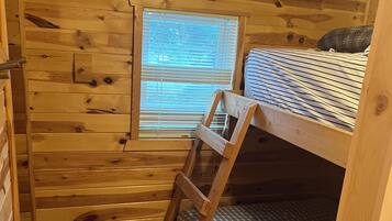 Una stanza in legno con un letto a castello, una finestra con persiane e un pavimento rivestito di moquette.