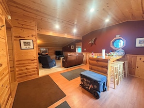 Ein gemütliches Blockhaus-Interieur mit Holzbalkendecke, einem Ledersofa, einer kleinen Bar und einem Fenster mit Blick.