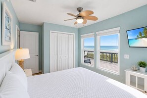 A bedroom with a bed, a ceiling fan, a window with a view of the beach, and a TV on the wall. - 1st Ashore – Beachfront St. George Island Vacation Rental (Saint George Island)