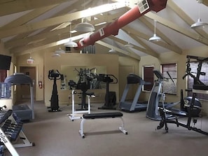 Ein Fitnessstudio mit unterschiedlichen Trainingsgeräten, darunter Laufbändern und Kraftmaschinen, unter einer geneigten Decke mit freiliegenden Balken.