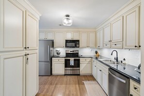 Une cuisine avec des meubles blancs, des appareils en acier inoxydable et un plancher en bois.