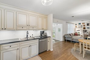 A modern kitchen with white cabinetry, a black countertop, and a built-in dishwasher. - Renovated 4BR Home on James Island | Minutes to Do (Charleston)