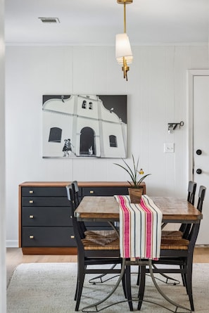A dining area with a table, chairs, a bench, a potted plant, and a wall-mounted picture. - Renovated 4BR Home on James Island | Minutes to Do (Charleston)