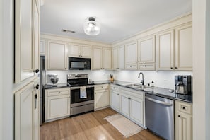 A kitchen with white cabinets, stainless steel appliances, and a wooden floor. - Renovated 4BR Home on James Island | Minutes to Do (Charleston)