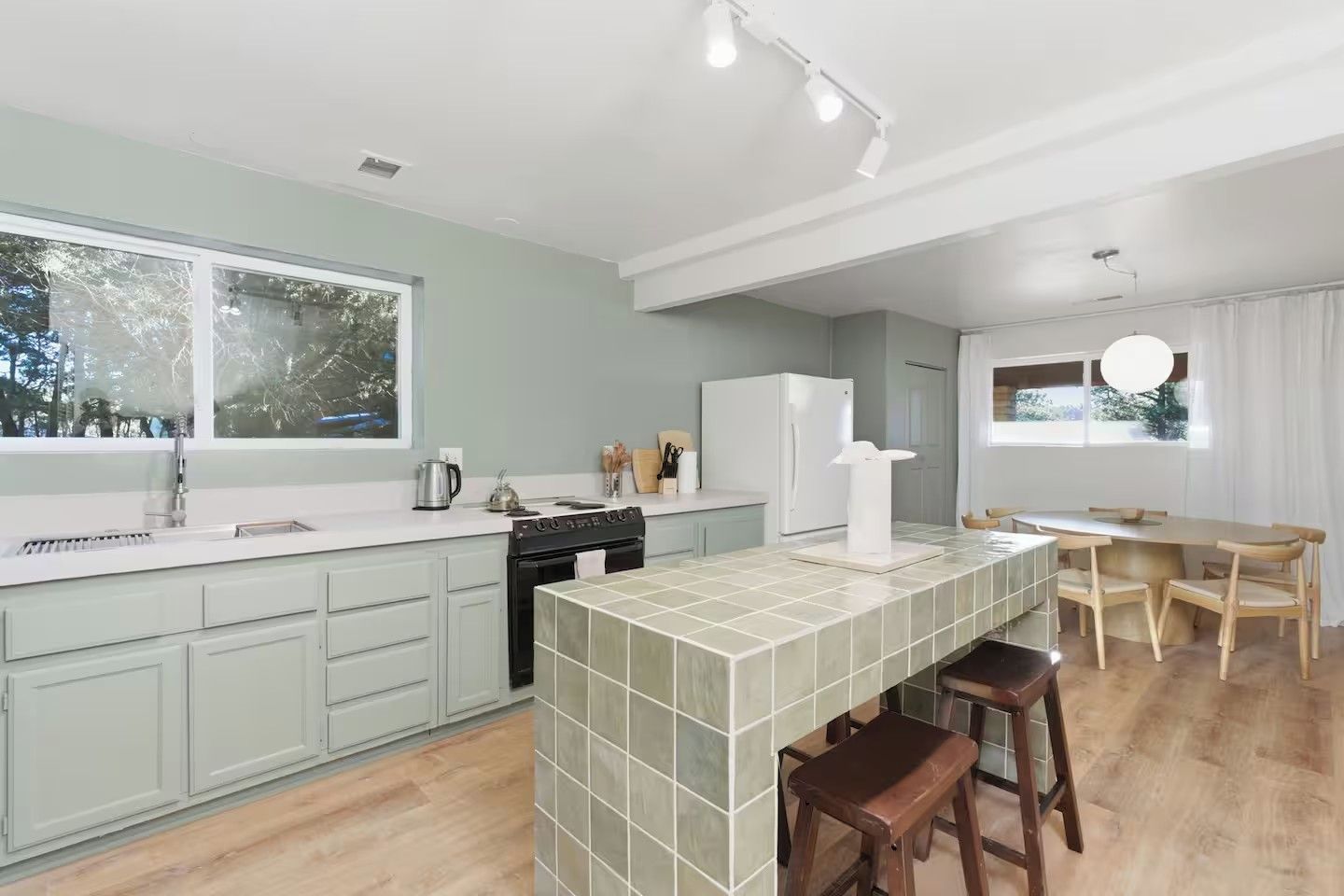Una cocina moderna con una isla central, una zona de comedor con mesa y sillas, y vistas al exterior a través de grandes ventanales.