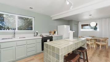 Una cocina moderna con una isla central, una zona de comedor con mesa y sillas, y vistas al exterior a través de grandes ventanales.