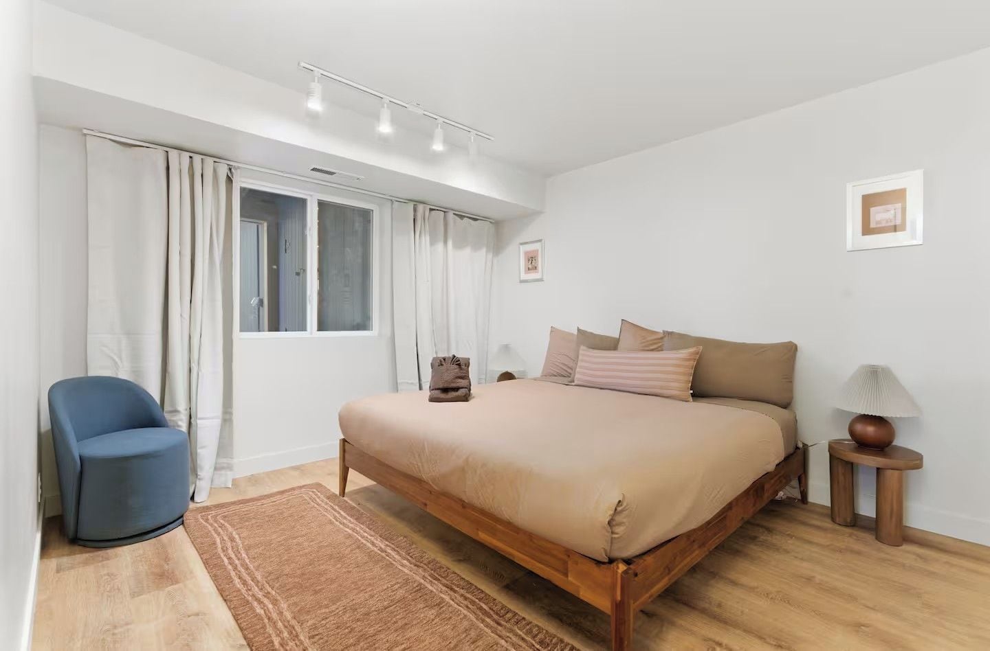 Un dormitorio con cama, una silla, una mesita de noche con lámpara y una ventana con cortinas.