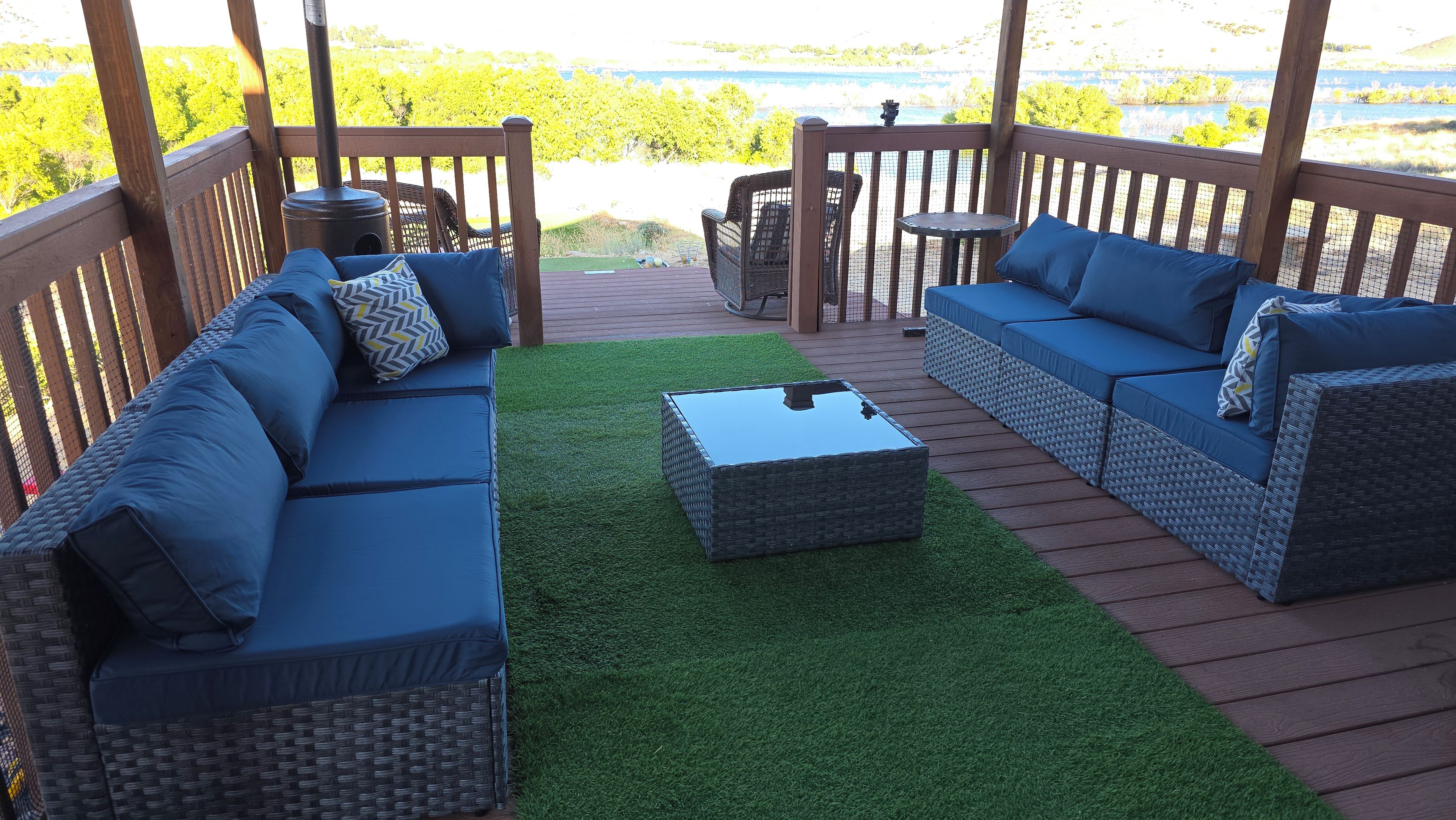 A covered outdoor seating area with wicker furniture and a glass-top coffee table, overlooking a body of water.
